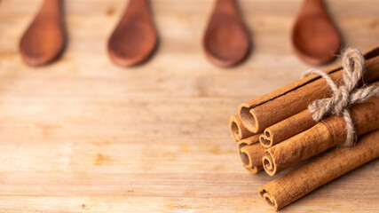 close up of cinnamon sticks and wooden spoons kept on a wooden chopping board, empty spoons restaurant spoons