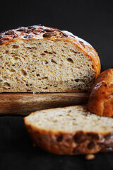 Fresh grain bread next to cut pieces on a wooden board on a dark background