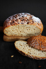 Fresh grain bread next to cut pieces on a wooden board on a dark background