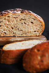 Fresh grain bread next to cut pieces on a wooden board on a dark background