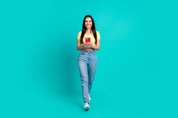 Full size photo of nice young woman walk use phone wear top isolated on teal color background