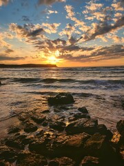 Naklejka premium Sunset at the beach, with stones formation and cloudy dramatic sky