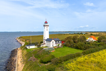 Aerial drone image of white Danish lighthouse Heln&aelig;s Fyr on island with yellow rape seed fields along coast shore, in Baltic sea the little belt, strait and cottage house