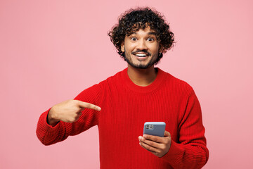 Young shocked surprised Indian man he wear red sweater casual clothes hold in hand use point finger...