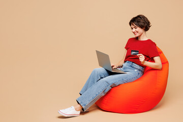 Full body young IT woman wear red t-shirt casual clothes sit in bag chair using laptop pc computer...