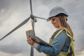 A skilled female engineer analyzes data at a wind turbine site, demonstrating her expertise in...