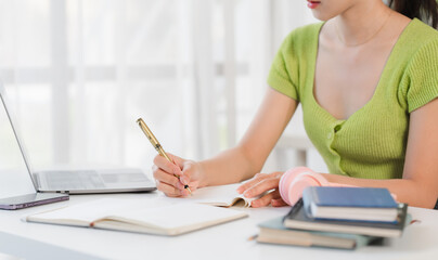 Focused Student:  A young woman diligently taking notes, surrounded by books and a laptop,...