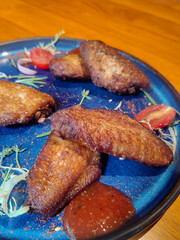 Grilled spicy chicken wings with ketchup on a black plate on a dark slate, stone or concrete background.