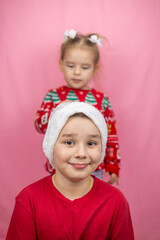 Brother and sister in festive Christmas attire, eagerly preparing for Christmas on a pink background. Cute children sincerely rejoice at the coming of Christmas and New Year.