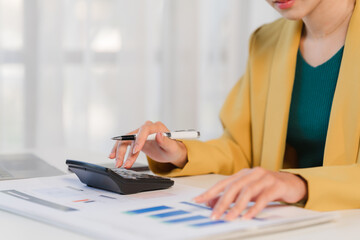 Focused Financial Analysis: A close-up shot of a businesswoman meticulously reviewing financial documents and using a calculator, showcasing dedication and precision.
