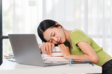 Exhausted Student Napping on Books: A young woman, overcome by fatigue, rests her head on a stack of books next to her laptop.  The image captures the exhaustion of a student's life.