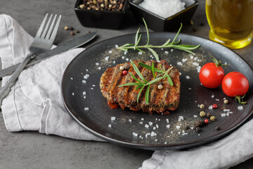 Black Angus Eye of round steak marinated and grilled  on black retro plate with rosemary herb, spices and cherry tomatoes