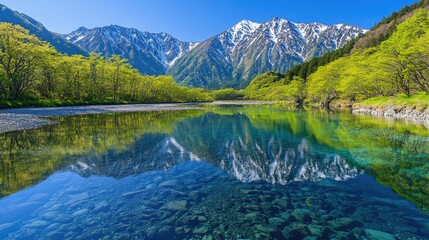 Fototapeta premium Crystal-clear waters of the Azusa River reflecting the vibrant greenery and majestic Hotaka Mountains, showcasing the natural beauty of Kamikachi in spring.
