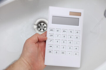 Hand holding calculator over the sink. Water consumption, savings