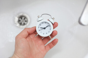 hand holding alarm clock over a sink with flowing water
