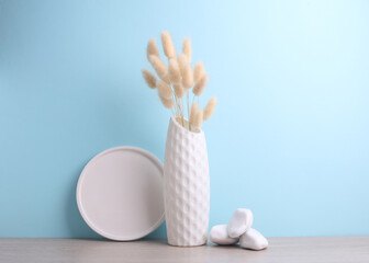 Minimalistic vase in Scandinavian style with dried lagurus flower and plaster ptate, stones on the table, blue background