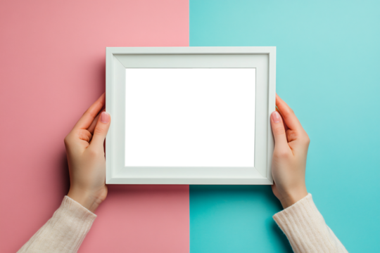 Woman's hands holding white empty picture frame on blue and pink background. Inside of picture transparent or white