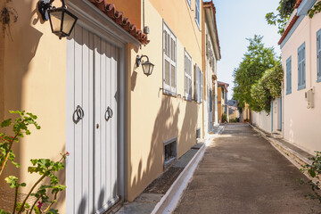 Wander through a picturesque alley in Nafplio, Greece, where pastel-colored houses line the cobbled path, adorned with vibrant flowers and serene greenery.