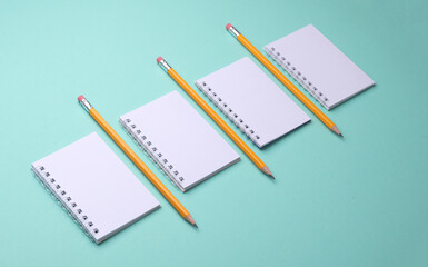 Blank white spiral notebooks with pencils on mint green background