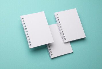 Group of white blank spiral notebooks on mint green background