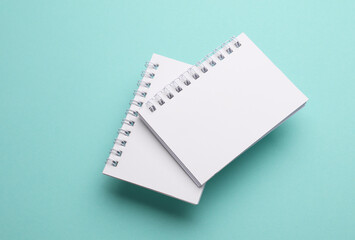 Two white blank spiral notebooks on mint green background