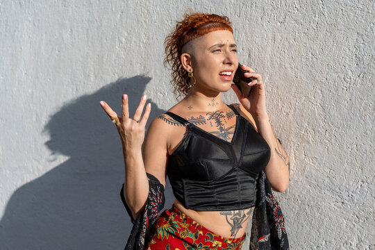 Frustrated woman talking on smartphone at wall