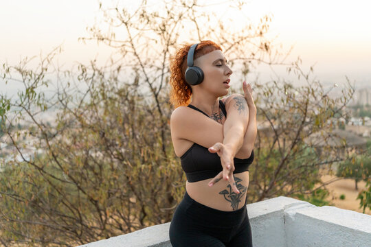 Woman in headphones doing stretching exercise at sunset
