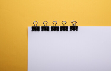 White sheet of paper with binders on yellow background