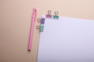 White sheet of paper with colored binders and pen on beige background