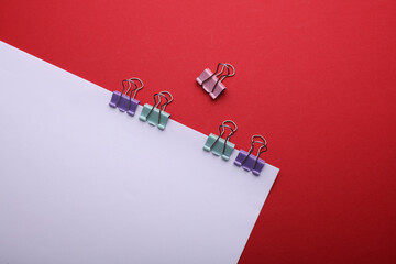 White sheet of paper with colored binders on red background