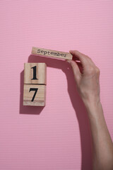 Hands holding wooden block calendar with date September 17 on pink background