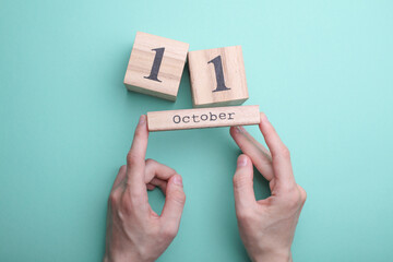 Hands holding wooden block calendar with date october 11 on mint green background