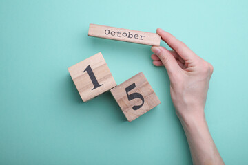 Hand holding wooden block calendar with date october 15 on mint green background