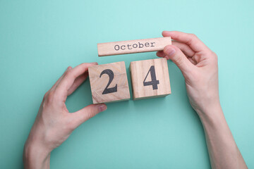 Hands holding wooden block calendar with date october 24 on mint green background