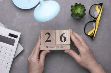 Hands holding a wooden block calendar 26 November against the background of a work space. Top view