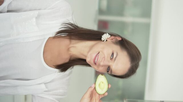 Vertical video, a woman brings an avocado to her face.