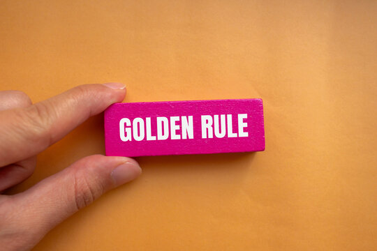 Golden rule message written on pink wooden block with orange background. Conceptual golden rule symbol. Copy space.