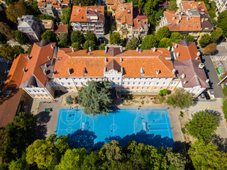 Naklejka premium Aerial view of a schoolyard basketball and sports court surrounded by trees and buildings, creating a vibrant and active urban space. Perfect for education or urban planning visuals
