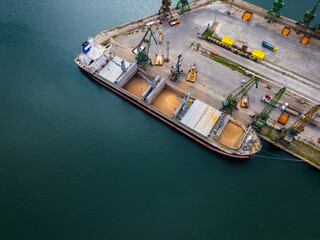 Aerial view of a cargo ship in a harbor uploading grains in a busy port during daylight hours