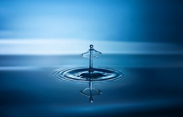 A single water drop falls onto a surface, creating a crown-like splash and ripples.