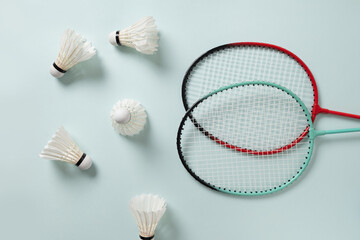 White feather badminton shuttlecocks and two badminton rackets on light blue background. View from above. Concept racket sport. Leisure games.