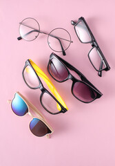 Assorted sunglasses and eyeglasses on a pink background