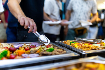 People enjoying a buffet meal with various dishes and fresh vegetables at a social gathering in a lively setting