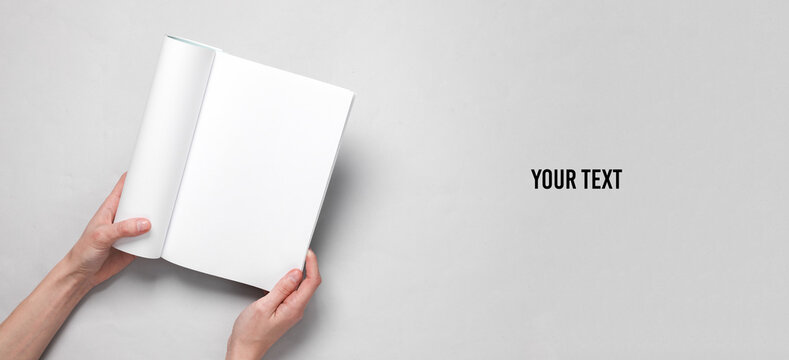 Women's hands hold magazine or catalog with an open blank white page on a gray background. Template for design, mockup, copy space