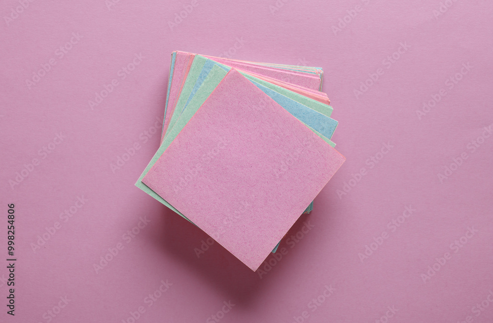 Wall mural stack of colored square memo sheets of papers on pink background. top view