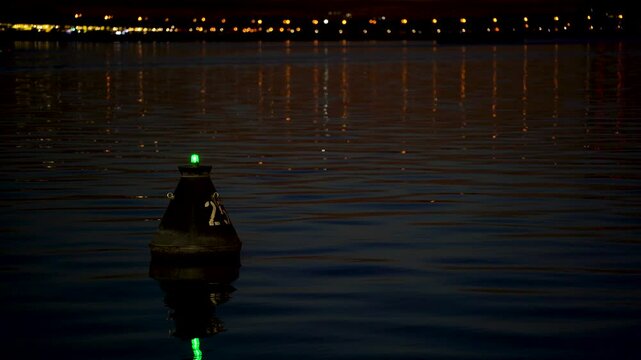 A boat sails past a buoy at night on the water