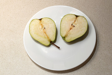 Two halves of a green pear. A juicy green pear cut in half on a white plate on the kitchen table,...