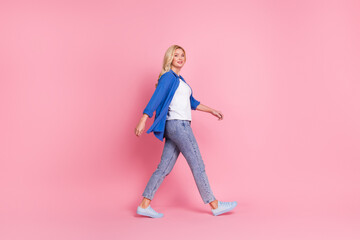 Full length photo of pretty positive woman wear blue shirt walking empty space isolated pink color background
