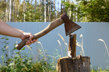 A man's hand holds an old rusty axe used for chopping firewood