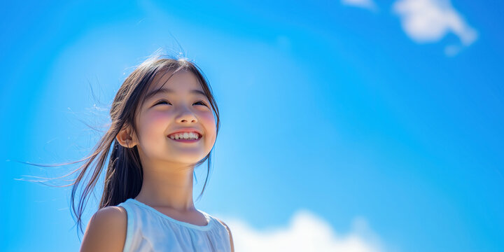 Looking up and smiling asian child, closeup portrait with blue bright sky on the background. Summer vacation concept template.